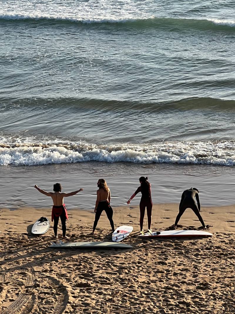Four surfers warming up on the beach next to their boards before going in the water