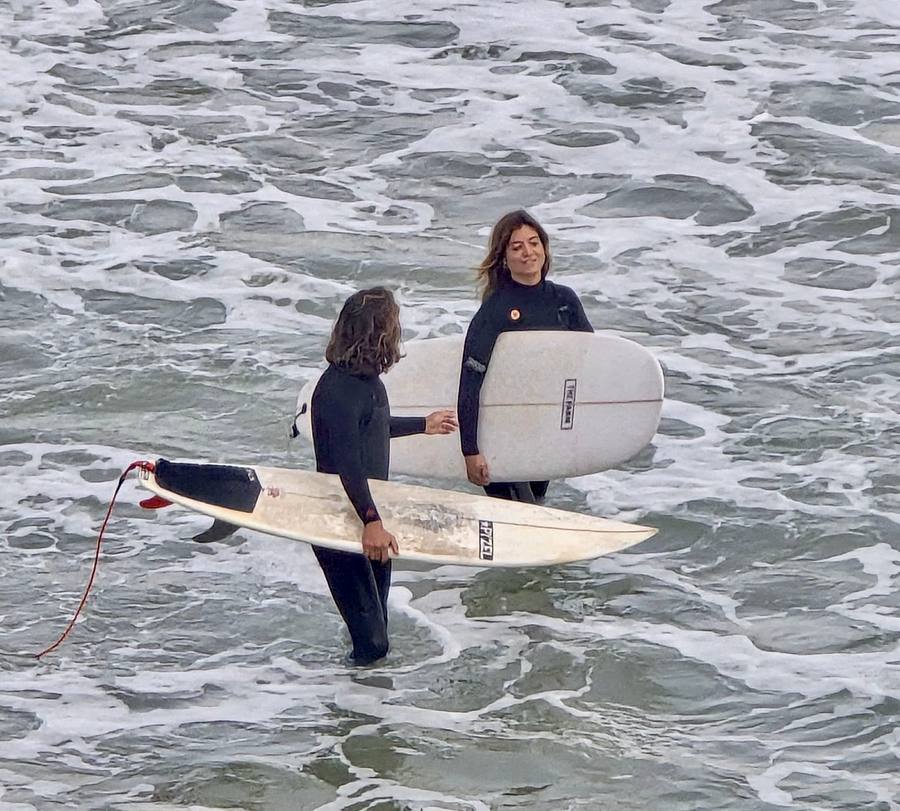 Instructor talking with a smiling student in the white water, both holding their boards