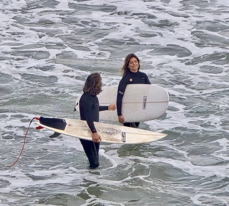 Instructor talking with a smiling student in the white water, both holding their boards