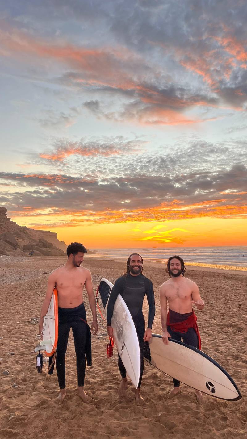Three friends smiling on the beach with their surfboards at sunset
