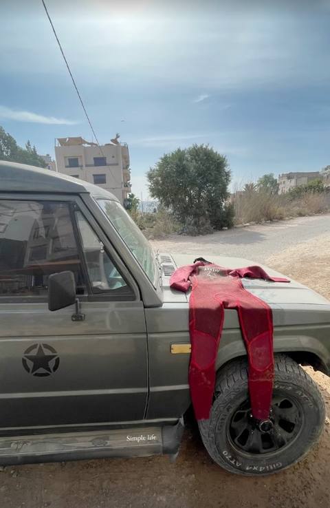 A red wetsuit drying on the bonnet of a 4x4