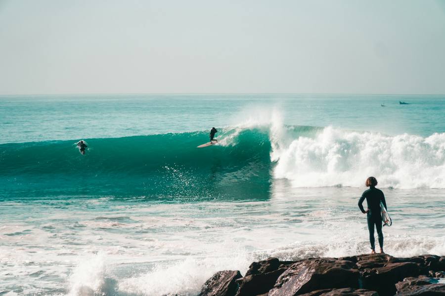 Surfer riding a long right-hand wave at Anchor Point, Taghazout, Morocco, while another watches from the rocks