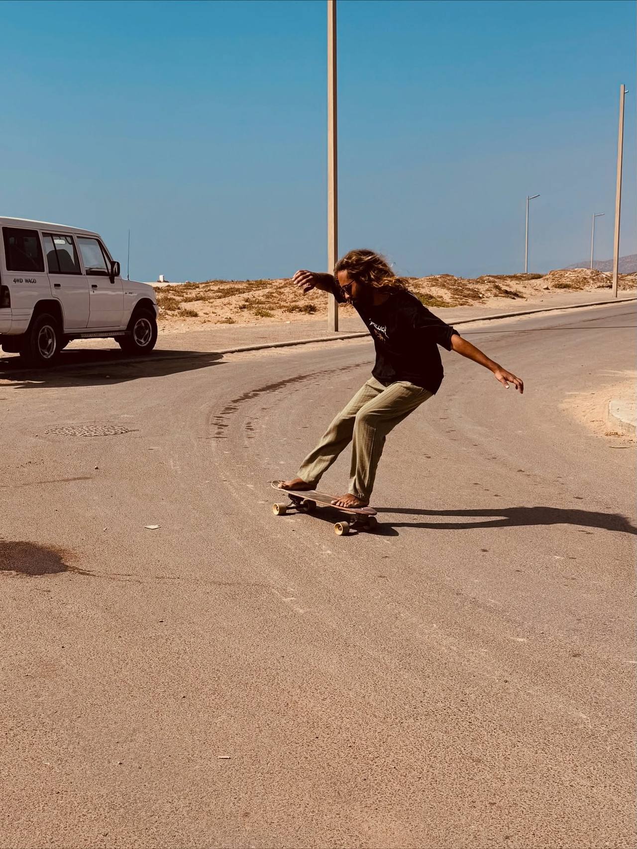 Surfer riding a surf skate on a sandy road by the sea, arms out