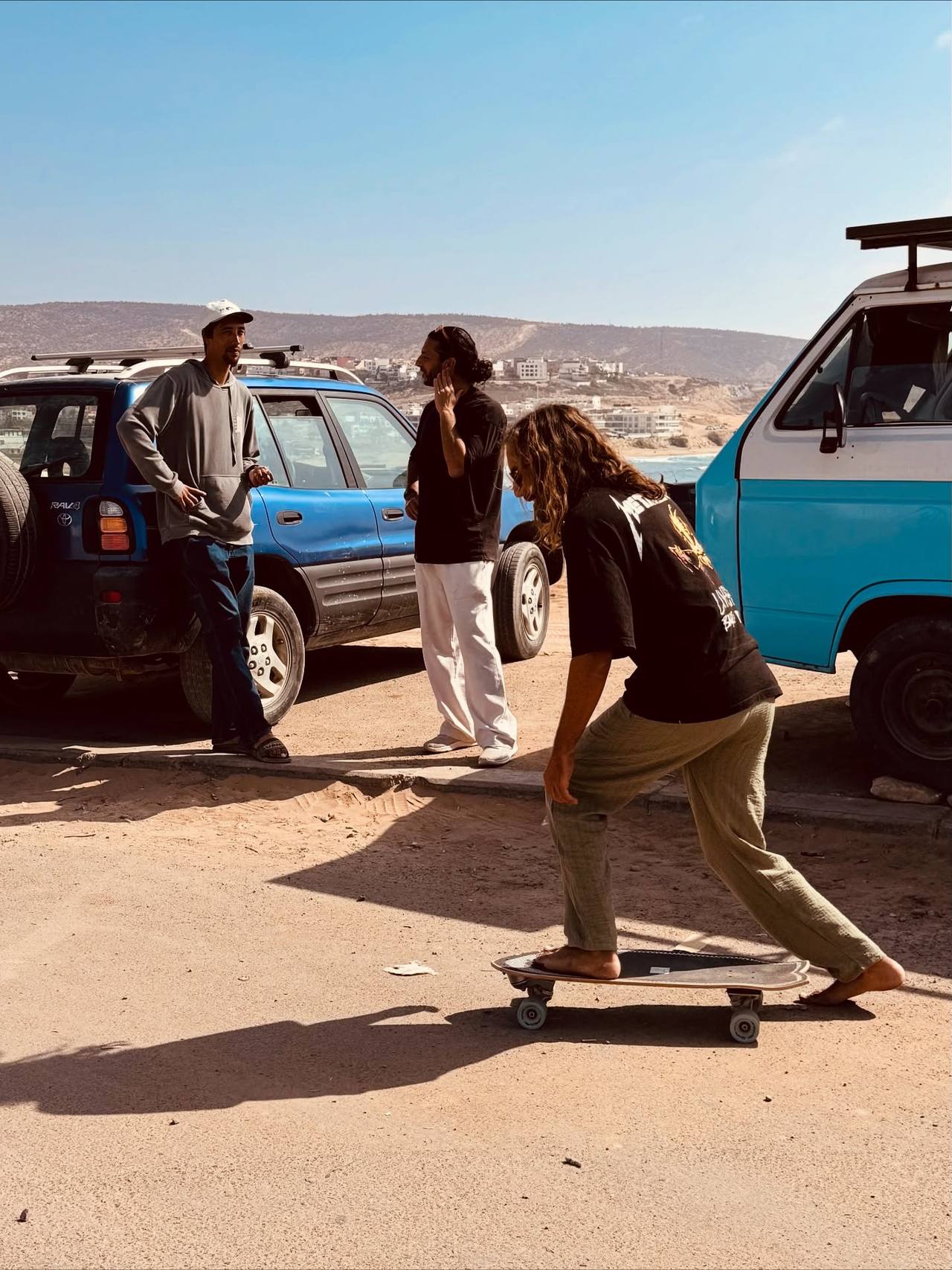 Surfer riding a surf skate past the vans and 4x4s parked above the beach