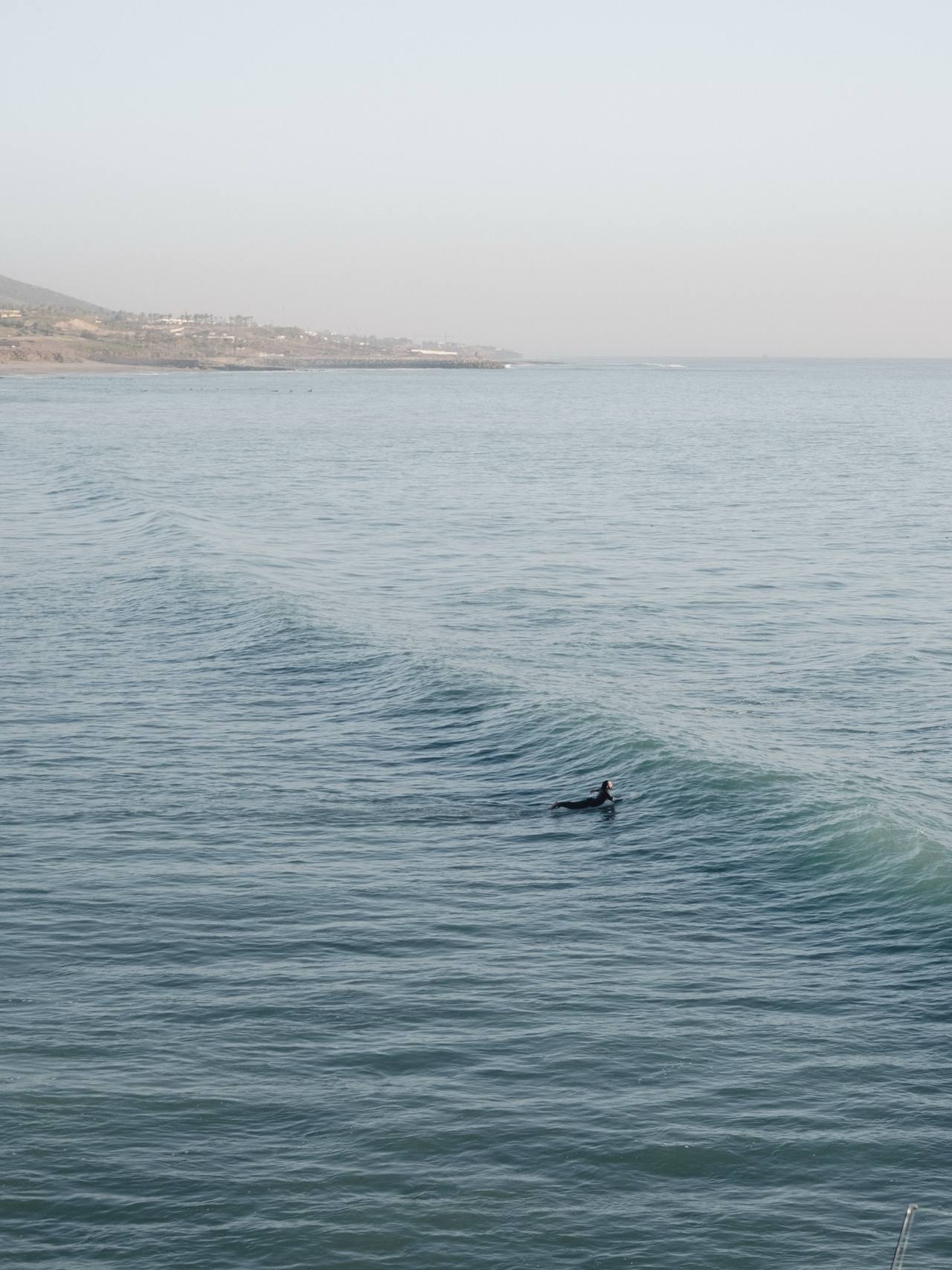 A lone surfer riding a long wave along the bay, hills in the distance