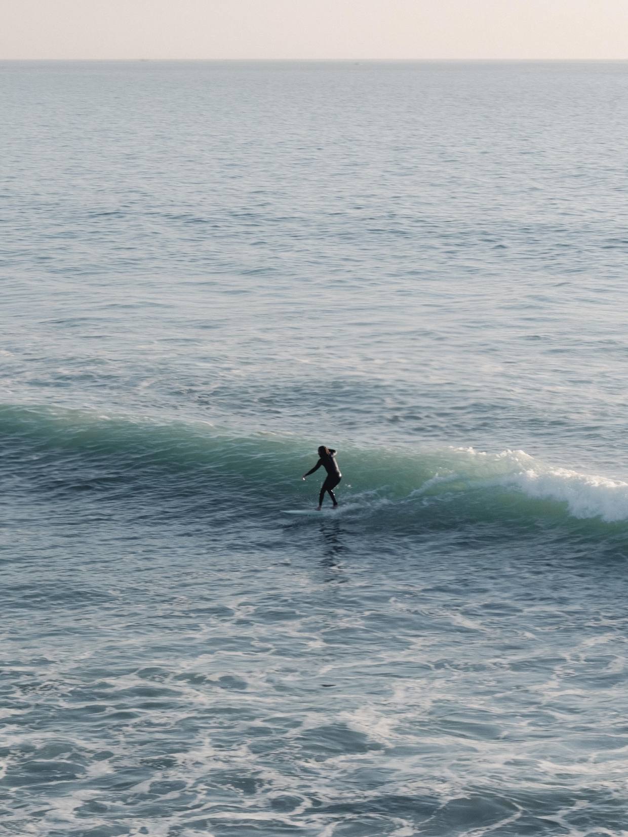 Surfer riding a small green wave on a calm morning sea