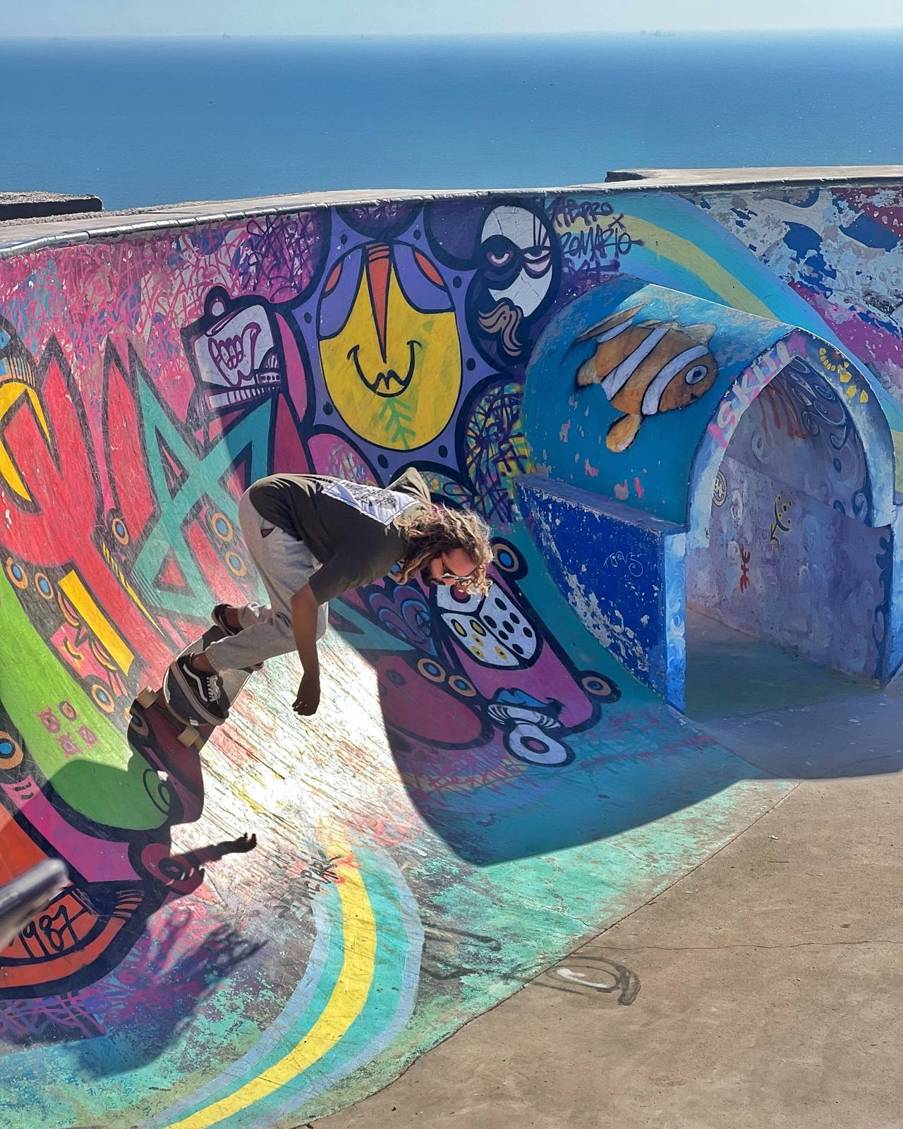 Surf skater carving a colourful painted bowl above the ocean
