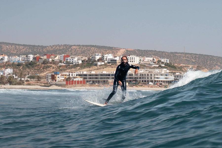 Surfer riding a wave in front of the hillside village of Tamraght