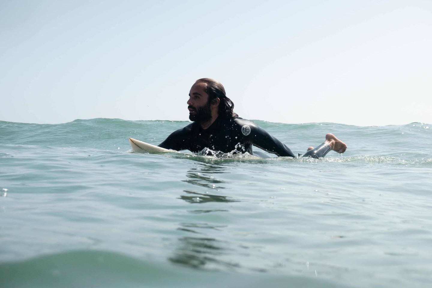 Nouamane, co-founder and surf instructor at Playtide Surf School in Tamraght, lying on his board in the water